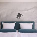 Schlafzimmer mit Bett und Wandbild eines Surfers auf Wellen.