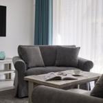 Ein Wohnzimmer mit grauem Sofa, Holztisch und Fernseher an der Wand.