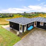 Moderne Villa mit Terrasse und blauem Surfbrett. Blick auf grüne Landschaft und Ferienhäuser.