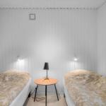 Zwei Einzelbetten mit Tisch und Lampe in einem Raum mit weißen Wänden.