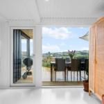 Durchgehende Glasschiebetüren führen auf eine Terrasse mit Tisch, Stühlen und Grill.