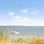 Ein weißes Boot liegt im Wasser vor einer Küstenlandschaft unter blauem Himmel.