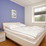 Schlafzimmer mit Bett, Nachttisch und Fenster. Wand in Blau. Holzfußboden.