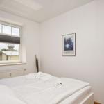 Ein Schlafzimmer mit weißem Bett, Fenster und Bild an der Wand.