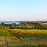 Panorama über Felder, Bäume und Meer unter klarem Himmel.
