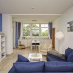 Wohnzimmer mit blauem Sofa, TV und Essbereich mit Tisch und Stühlen.