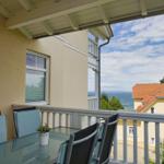 Terrasse mit Tisch und Stühlen. Blick auf das Meer und ein Haus.