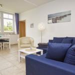 Wohn- und Essbereich mit Sofa, Tisch und Stühlen. Fenster mit Blick auf Grün.