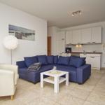 Wohnbereich mit blauem Sofa, weißem Tisch und Küchenzeile.