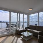 Wohnzimmer mit Blick auf den Hafen und Terrasse mit Tisch und Stühlen.