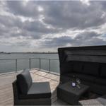 Terrasse mit Sitzgruppe und Blick auf Wasser und Himmel.