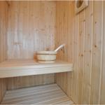 Sauna mit Holzbank und Eimer. Holzwand und Uhr sichtbar.