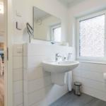 Badezimmer mit Waschbecken, Spiegel und Fenster. Im Hintergrund ist das Wohnzimmer sichtbar.