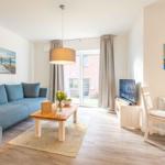 Wohnzimmer mit Sofa, Esstisch und TV. Tür führt auf Balkon.