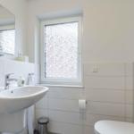 Badezimmer mit Waschbecken, Toilette und Fenster mit beschichtetem Glas.