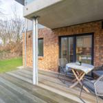 Terrasse mit Tisch und Stühlen, Blick in die Küche, Holzdecke und Backsteinwand.