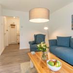 Wohnzimmer mit blauem Sofa, Holztisch und Küchenbereich im Hintergrund.