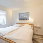 Schlafzimmer mit Doppelbett, Wandbild und Kleiderschrank.