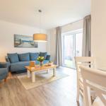 Wohn- und Essbereich mit Sofa, Sessel, Tisch und Fenster.