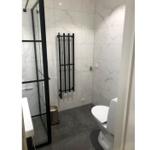 Bad mit Dusche, Toilette und Heizkörper an der Wand.