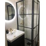 Badezimmer mit Duschkabine, Waschbecken und runden Spiegel mit Beleuchtung.