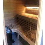 Sauna mit Holzbänken, Steinkachel und Eimer.