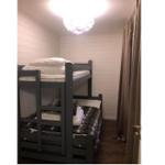 Zimmer mit Doppelstockbett, Holzboden und weißen Wänden. Deckenleuchte und Vorhang sichtbar.