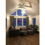 Wohnzimmer mit dunklen Sofas, Holzboden und hohem Dach. Fenster mit roter Sterndekoration.