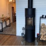 Schwarzer Kaminofen mit Holzstapel und Tisch im Eingangsbereich.