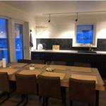 Essbereich mit Holztisch und Stühlen, Küchenzeile mit schwarzen Schränken und Fensterblick.