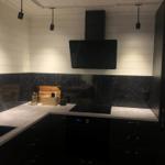 Küche mit schwarzen Schränken, Marmorwand und moderner Dunstabzugshaube.