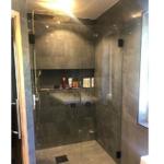 Duschkabine mit Glaswand und Duschkopf, dunkle Fliesen und integrierte Ablage