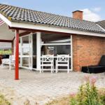 Haus mit Terrasse, weißen Stühlen und schwarzen Liegen. Roter Säulen und Ziegelmauer.