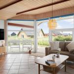 Wohnbereich mit Sofa, Couchtisch und Fernseher. Durchgehende Glasfront mit Blick auf Garten und Häuser.