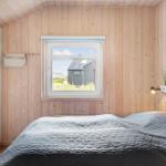 Schlafzimmer mit Holzwand, Bett und Fensterblick auf Außenbereich.