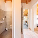 Badezimmer mit Toilette und Waschbecken. Durchgang zu Schlafzimmer und Dusche.