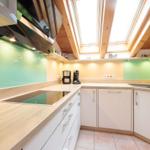 Küche mit Holzdecke, grüner Rückwand und Edelstahlgeräten.