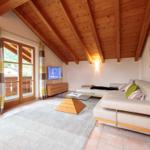 Wohnzimmer mit Holzdecke, Sofa, Couchtisch und Balkonansicht.