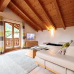 Wohnzimmer mit Holzdecke, Sofa, Glas-Tisch und Balkonansicht.