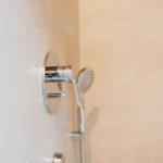 Dusche mit Chromarmatur und Handbrause an hellen Fliesen.