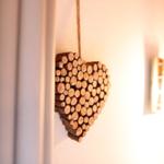 Ein Herz aus Holzstämmchen hängt an der Wand neben einer Lampe.