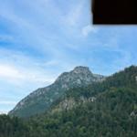 Blick auf einen bewaldeten Berg unter blauem Himmel mit weißen Wolken.