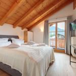 Schlafzimmer mit Balkon, Holzdecke und TV. Bett mit weißen Kissen.