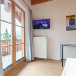 Zimmer mit TV, Balkon und Wandposter. Holzfußboden und weißer Heizkörper.