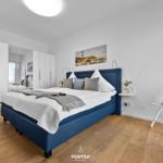 Schlafzimmer mit blauem Bett, weißen Wänden und Holzboden.