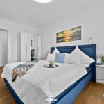 Schlafzimmer mit blauem Bett, Wandbild und Holzboden.