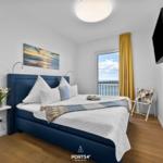 Schlafzimmer mit Blick aufs Meer, blauer Bettgestell und Wand-TV.