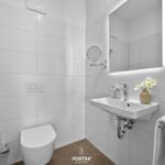 Badezimmer mit Toilette, Waschbecken und Spiegel. Weiße Fliesen und moderne Armaturen.