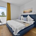 Schlafzimmer mit blauer Bettdecke, gelben Vorhängen und Blick aus dem Fenster.