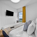 Schlafzimmer mit Blick aufs Meer, TV und gelbe Vorhänge.